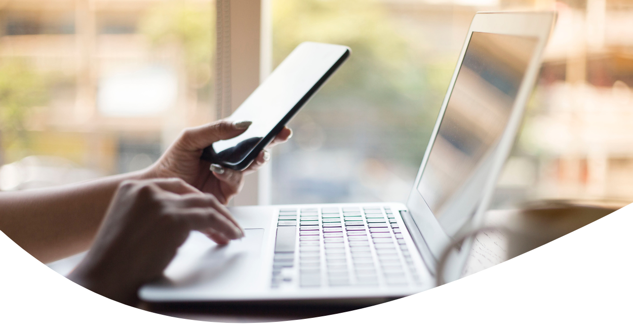 person working on laptop and holding cellphone