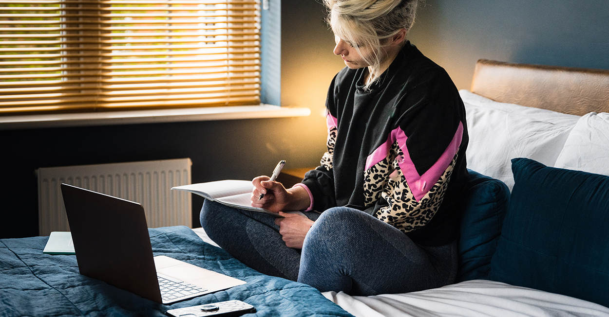 woman writing in notebook and working on laptop