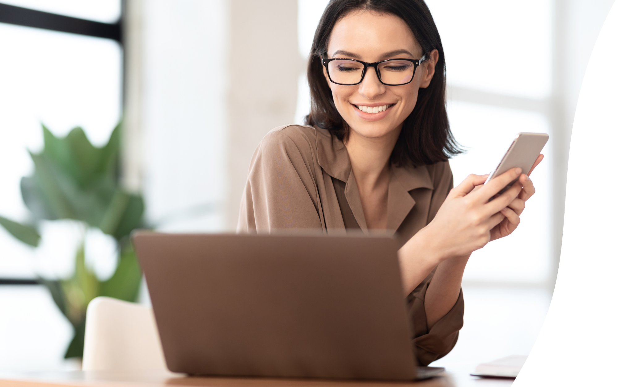 woman holding cellphone and working on laptop